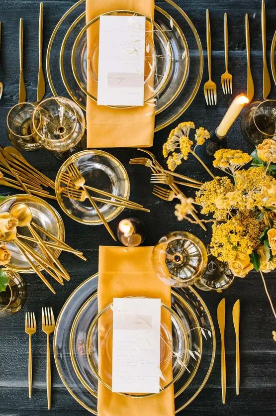 a bold and catchy spring tablescape with sheer glass plates, yellow napkins and blooms and gold cutlery is very modern