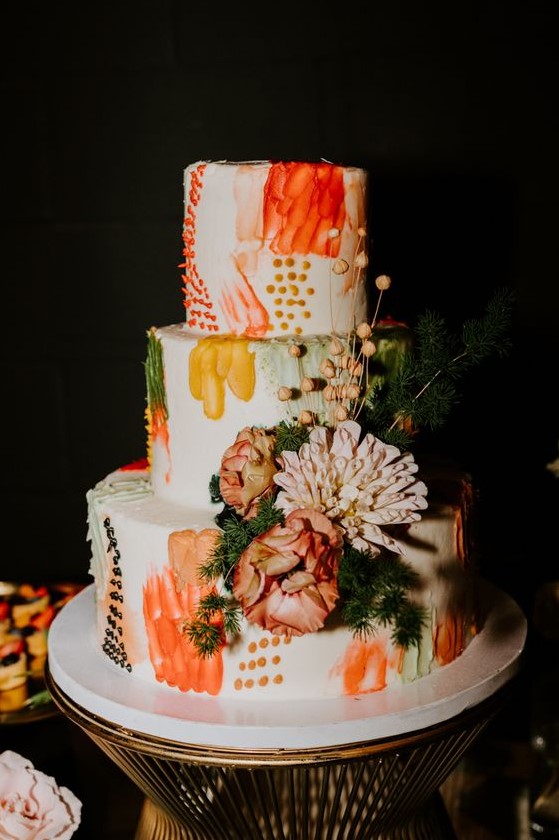 a bold color block wedding cake with orange, mustard, rust and green detailing, fresh blooms and berries and greenery