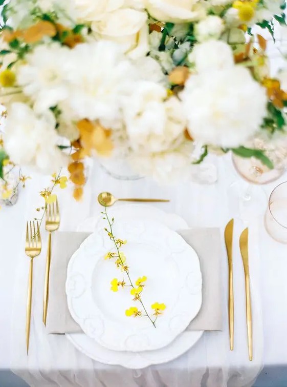 a bold spring wedding table setting with a grey napkin, a yellow blooming branch, gold cutlery and neutral blooms