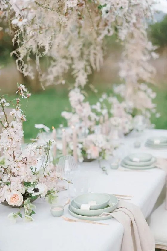 a breathtaking enchanted garden wedding tablescape done in pastel green and blush, with beautiful almond blossom centerpieces and green plates