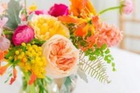a bright and pretty wedding centerpiece of orange, yellow, hot pink and peachy blooms, berries and greenery is amazing for spring or summer