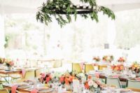 a bright spring wedding reception with a greenery chandelier, bright linens and chairs and colorful blooms