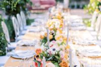 a bright spring wedding reception with colorful blooms and greenery, white candles, white linens and lots of greenery over the table