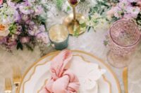 a bright spring wedding tablescape with lilac and pink blooms and greenery, gold-rimmed plates and gold cutlery, lilac candles and glasses