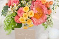 a bright wedding centerpiece of yellow, pink and white blooms and greenery is a cool solution for a spring or summer wedding