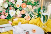 a bright wedding table setting with a yellow table runner, pink and red blooms, gold cutlery and a cookie