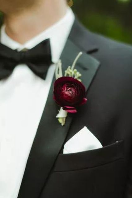a burgundy ranunculus with greenery is a bold touch of color and interest to the classic black suit