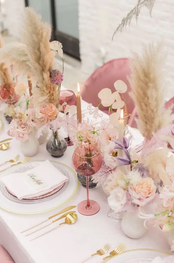 a cheerful spring wedding tablescape with pink glasses, pampas grass, gold cutlery and lilac blooms