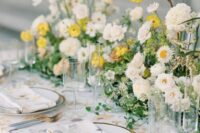 a chic and lush spring wedding tablescape with lush white and yellow blooms and greenery, gold-rimmed plates and gold cutlery