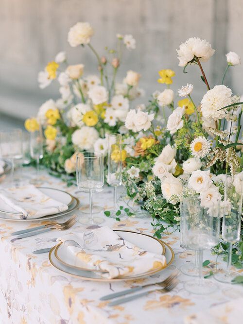 a chic and lush spring wedding tablescape with lush white and yellow blooms and greenery, gold-rimmed plates and gold cutlery