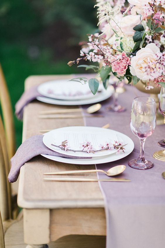 a chic mauve wedding tablescape with a lilac table runner and napkins, blush and pink florals, lilac glasses and gold cutlery