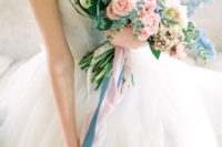 a chic pastel wedding bouquet of light pink and blue blooms and matching long ribbons for a spring bride