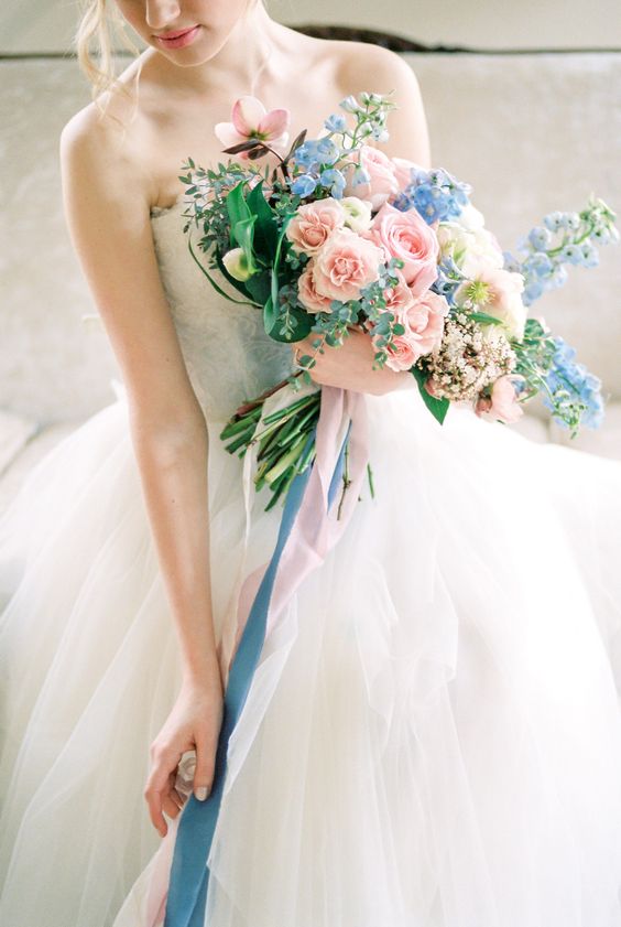 a chic pastel wedding bouquet of light pink and blue blooms and matching long ribbons for a spring bride