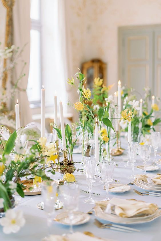 a chic spring wedding table setting with yellow and white blooms, white plates and linens, refined candleholders and vases