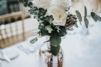 a chic wedding centerpiece of a mercury glass vase, greenery, berries, white roses is a very elegant and simple piece you can recreate