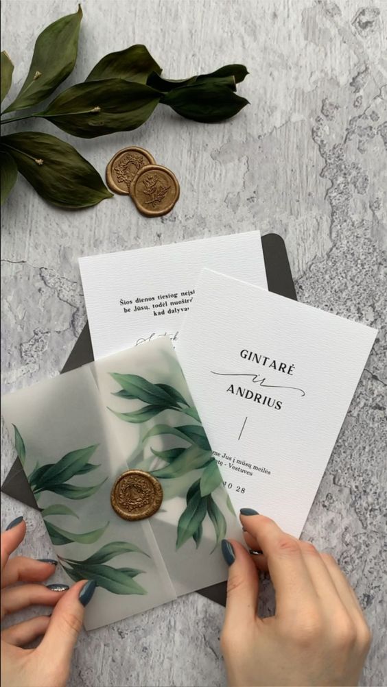 a chic wedding invitation suite with white invites, a semi-sheer envelope with painted leaves and a dark green envelope