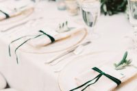 a chic wedding tablescape with creamy linens and green ribbons, a greeneyr runner and white blooms plus gold-rimmed glasses