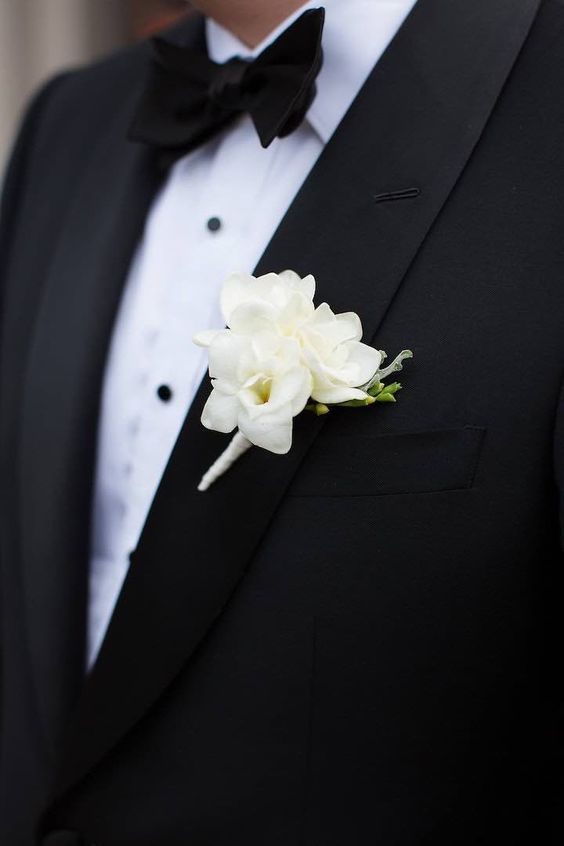 a classic black and white groom's look with a tux and a classic white winter floral boutonniere is a chic and refined idea for a modern and luxurious outfit