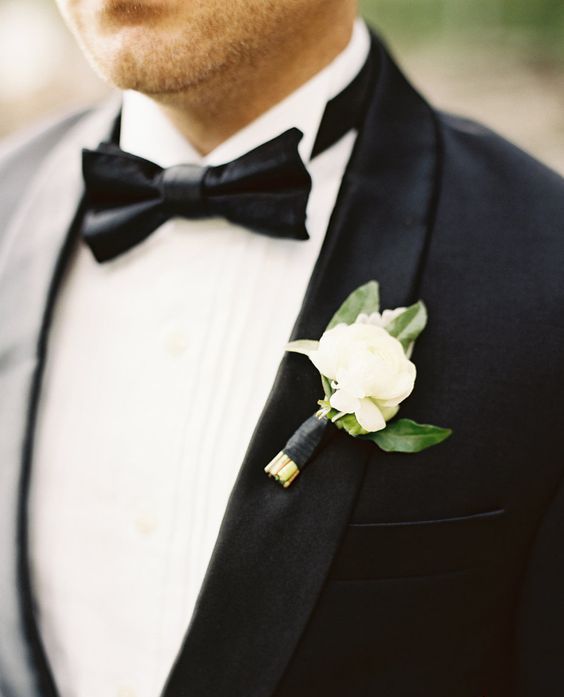 a classic black tux with a white peony boutonniere with some leaves and a black wrap is a stylish modern idea to rock