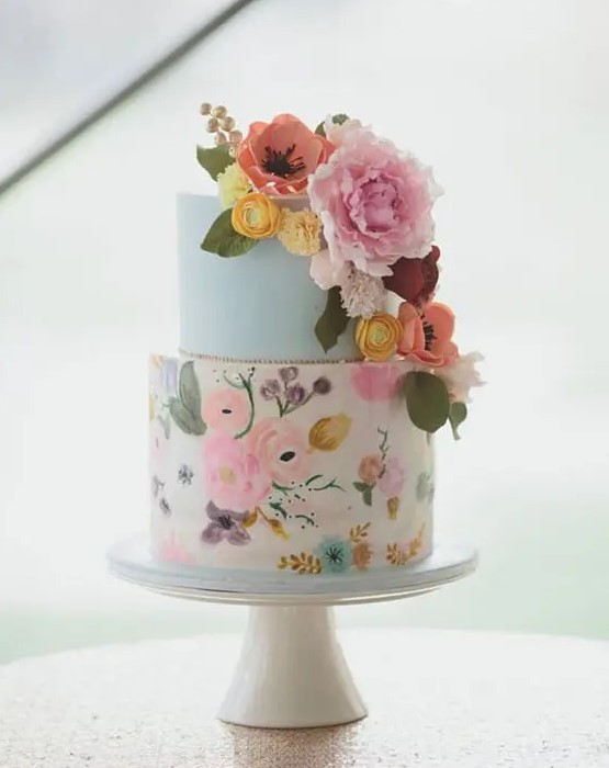 a colorful handpainted wedding cake with a light blue tier, a bright floral tier in various shades and sugar flower decor