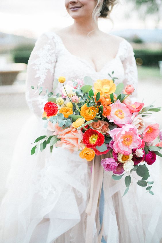 a colorful spring wedding bouquet with marigold, red and pink blooms plus greenery
