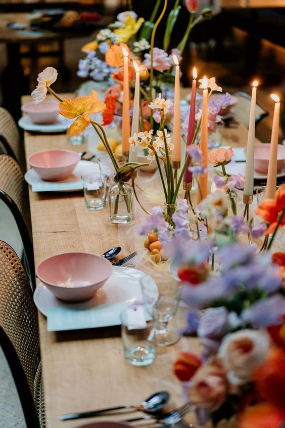 a colorful spring wedding tablescape with pink bowls, lilac, yellow, orange and peachy blooms and tall and thin candles