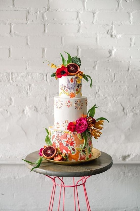 a colorful wedding cake with handpainted animals and birds, painted and fresh bold blooms, a cactus and some citrus