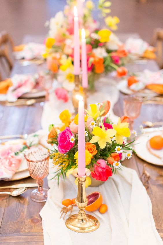 a colorful wedding tablescape with hot pink, coral, yellow blooms, pink tall and thin candles, pink glasses and napkins is gorgeous