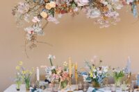 a cool and bright spring wedding tablescape with bright and pastel blooms, white and yellow candles, lavender glasses and an overhead floral installation