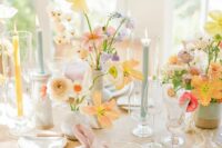 a delicate pastel spring wedding tablescape with pastel and muted color blooms, pastel candles, green plates and pink napkins