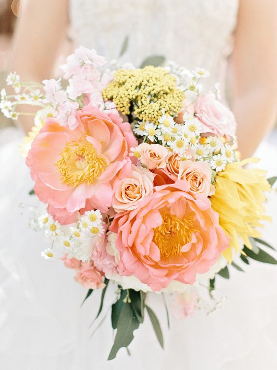 a delicate pastel wedding bouquet of blush, yellow and white blooms and berries plus some leaves for a spring bride