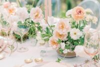 a delicate spring wedding table setting with blush and peachy plates and glasses, peachy and white blooms and blush candles