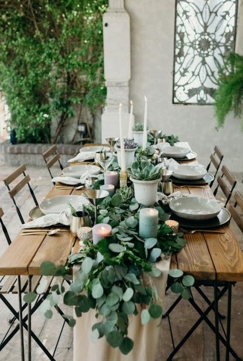 a eucalyptus table runner with succulents in pots, with pastel candles and tall white ones that match