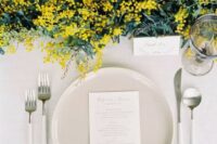 a fresh and sophisticated wedding tablescape with a mimosa and greenery runner, neutral plates, blue napkins