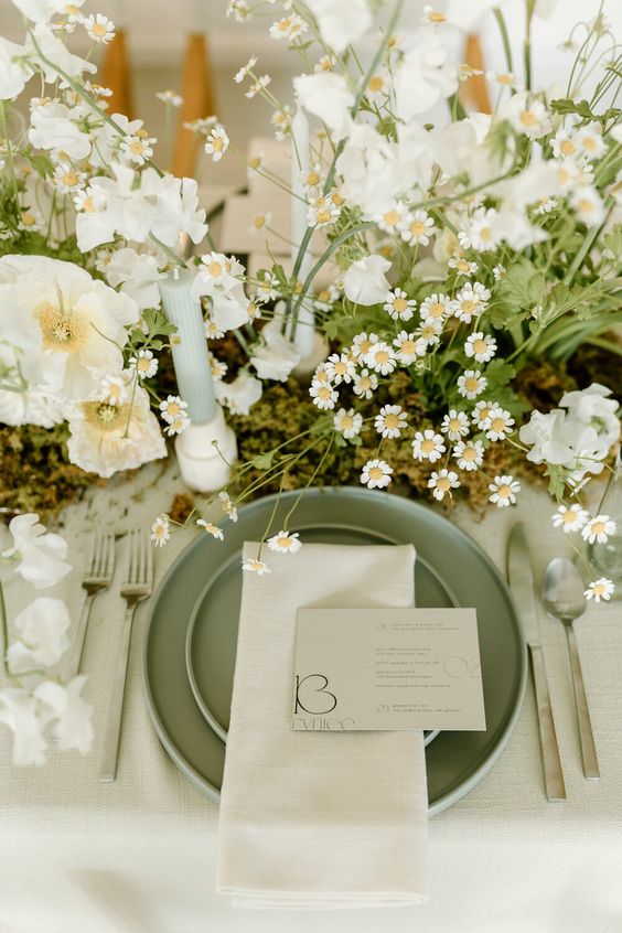 a fresh spring wedding table setting with white linens, green plates, pale green candles, fresh white blooms and moss