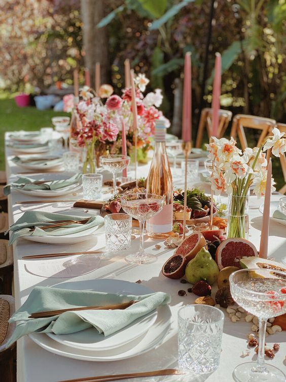 a fun and bright spring wedding tablescape with a neutral tablecloth and sage green napkins, bold blooms, pink candles, fruit on the table