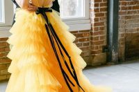 a gorgeous yellow A-line wedding dress with an open back, a tiered tulle skirt with a train and a black sash with a bow