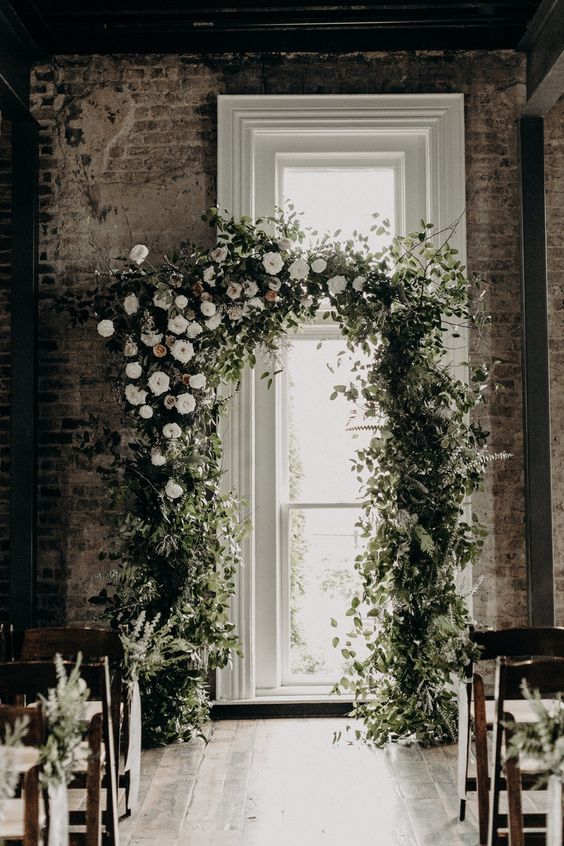 a lush greenery wedding arch with some white blooms is a textural and pretty idea for a spring or summer wedding