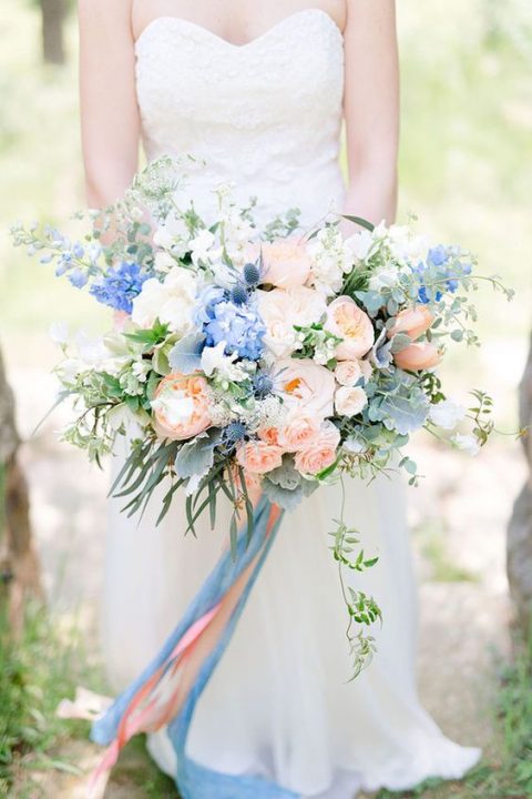 a lush wedding bouquet with peachy pink and blue flowers plus long ribbons for a pastel loving bride