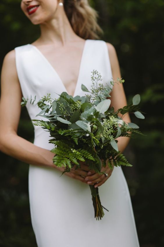 a minimalist white wedding dress with a deep neckline and a stylish fern and seeded eucalyptus wedding bouquet for a modern wedding
