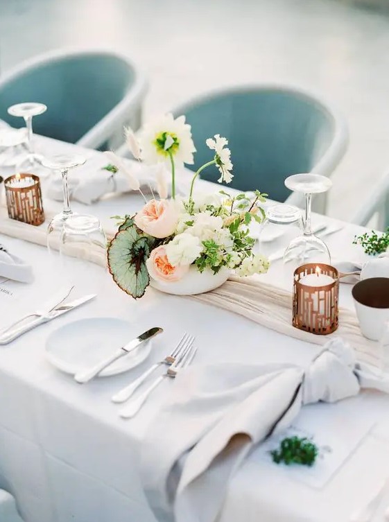 a modern and refined spring wedding table with neutral linens, candles, a catchy floral centerpieces and simple cutlery