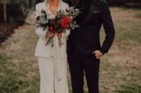 a modern boho bride wearing a white pansuit with a white shirt, a white hat and platform heels