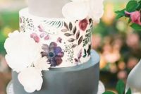 a modern wedding cake with two grey tiers and a floral painted tier in the center plus white sugar blooms
