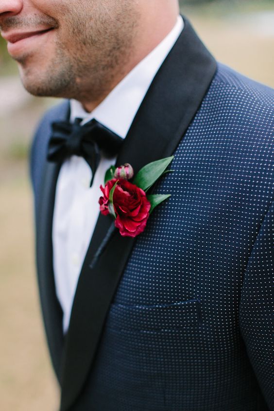 a navy polka dot tux with black lapels, a black bow tie and a bold red bloom and leaves for a lovely and bold touch of color