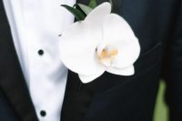 a navy tuxedo spruced up with a white orchid and greenery boutonniere is a stylish idea for a modern luxurious wedding