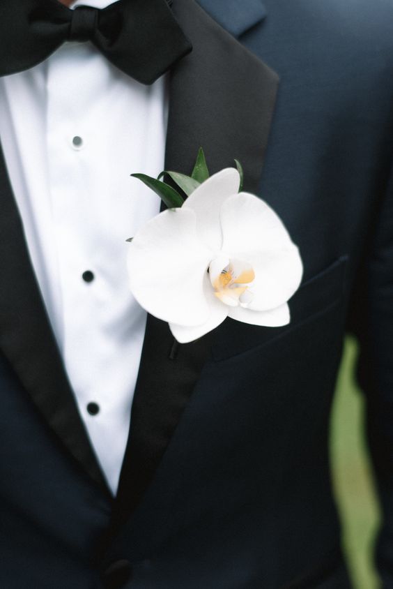a navy tuxedo spruced up with a white orchid and greenery boutonniere is a stylish idea for a modern luxurious wedding