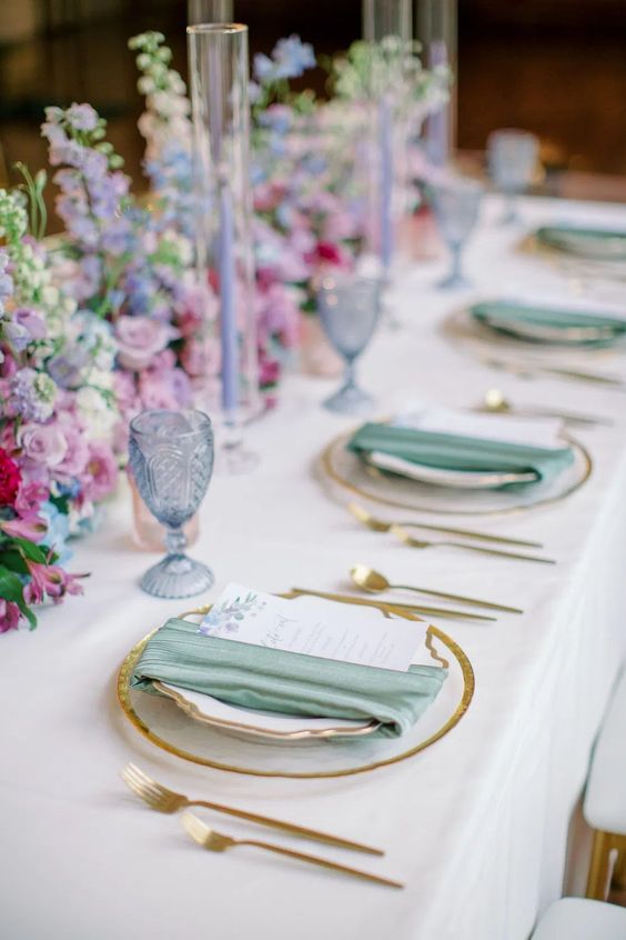 a pastel spring wedding tablescape with lilac and pink blooms, lilac candles, gold-rimmed plates and green napkins