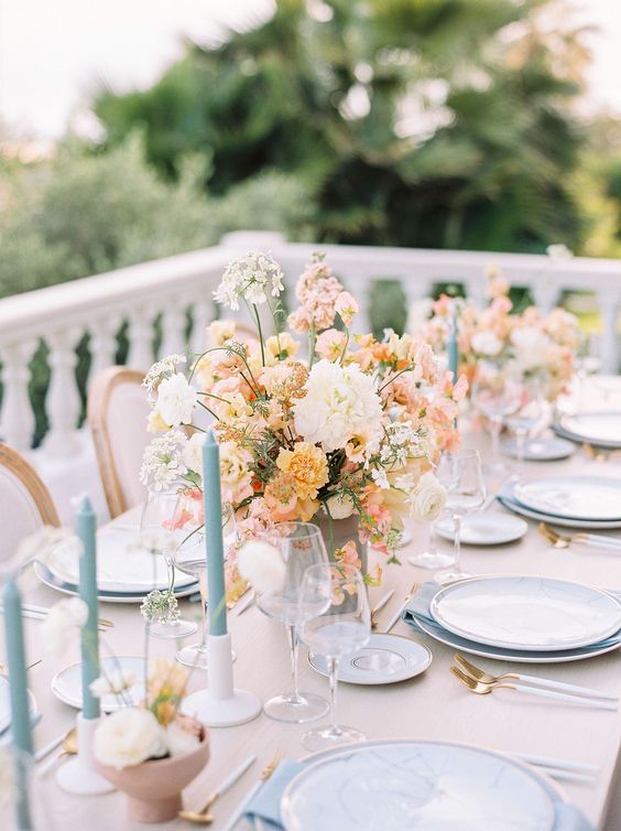 a pastel spring wedding tablescape with neutral and pastel blooms, dusty blue candles and blue napkins plus blush plates