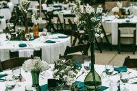 a pretty green and white wedding table with a cluster wedding centerpiece with white blooms and green vases, hunter green napkins and a white tablecloth