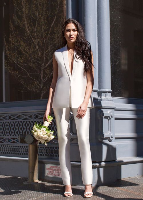 a pure white pantsuit with a sleeveless vest with a plunging neckline and pants, heels and minimalist earrings